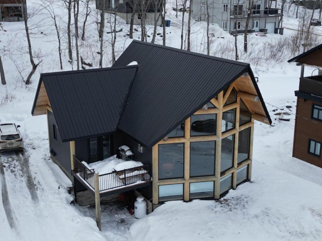 a house with a black roof in the snow at Chalet en montagne - Spa et Ski - Le Goathouse in Saint-Philémon