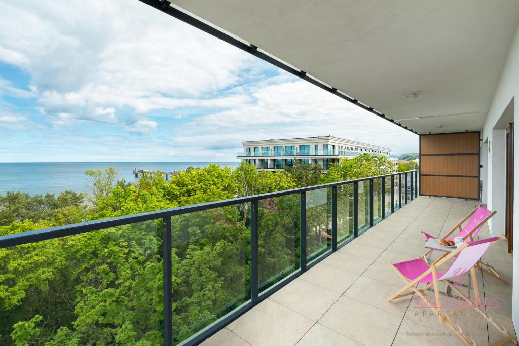 Un balcón con una silla rosa y el océano. en Your Holidays Aquamarina Prima 60, en Międzyzdroje