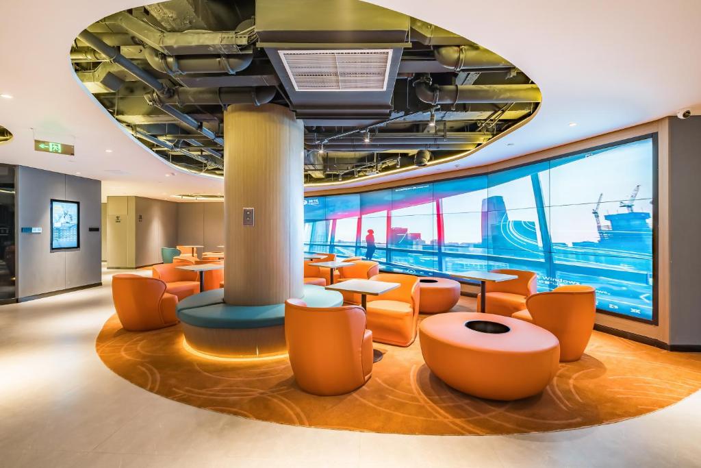 eine Lobby mit orangefarbenen Stühlen und Tischen und einem großen Fenster in der Unterkunft VYLUK Hotel Beijing Universal Studios-蔚徕酒店 北京环球影城店 in Peking