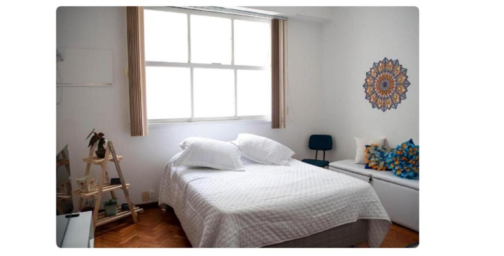 a bedroom with a bed with white sheets and a window at Apto Centro do Rio - Cinelândia - Consulado Americano - Vivo Rio - 1 min Metrô in Rio de Janeiro