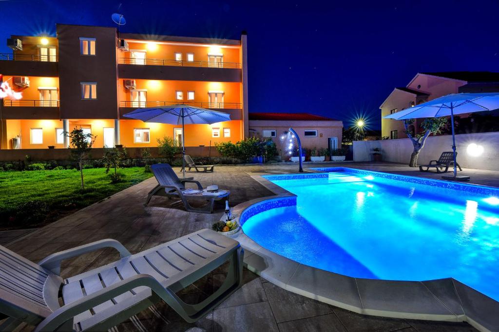 una piscina por la noche con sillas y sombrillas en Apartments Bonex, en Privlaka
