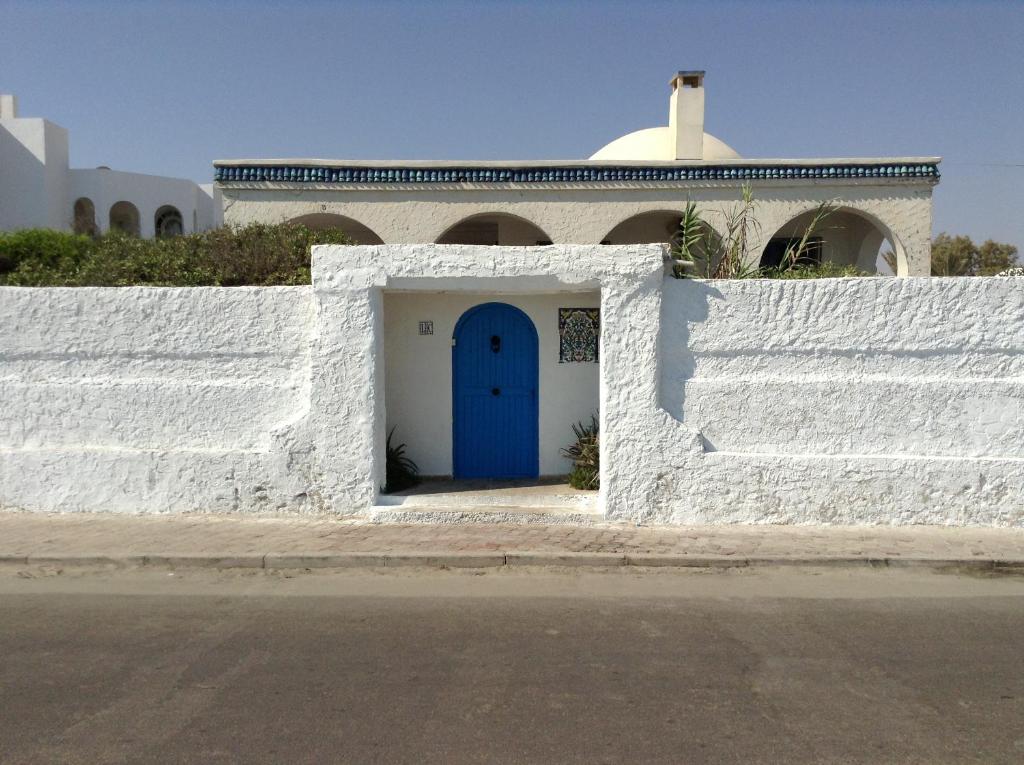 a white fence with a blue door in front of a building at La Brise de Djerba, Villa de Charme en bord de mer à Al Jazira in Mezraya