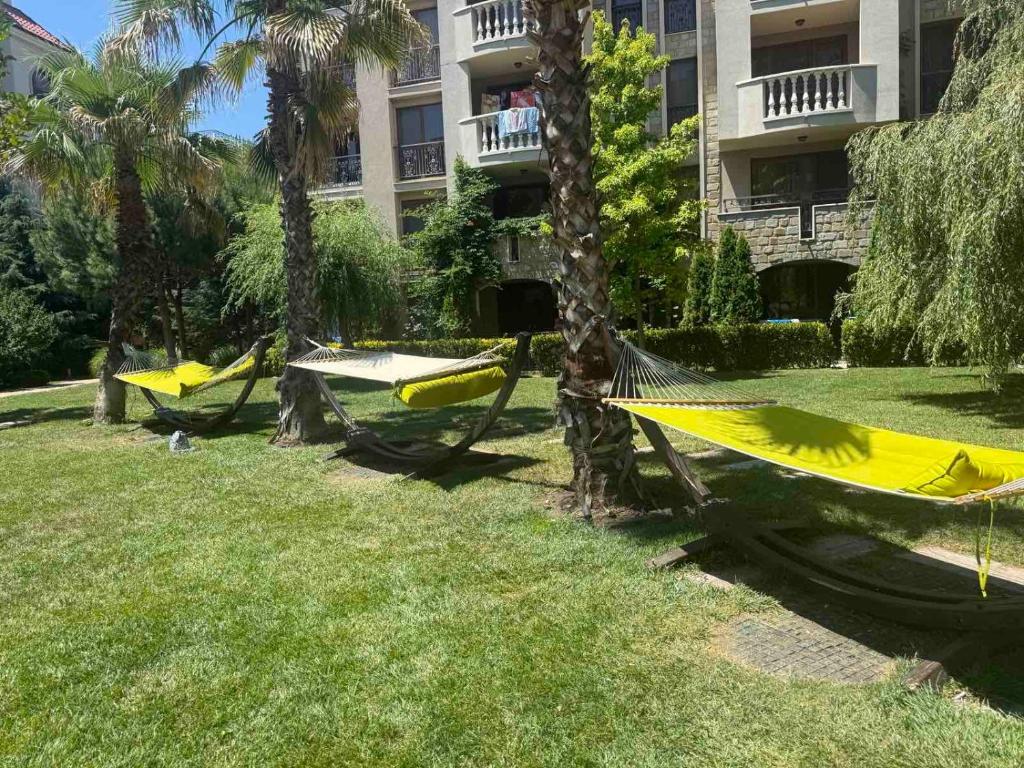 three hammocks in a park with palm trees and a building at Flat in Cascadas 21 in Sunny Beach