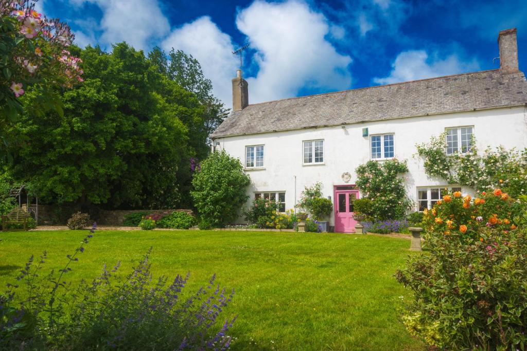 a white house with a red door on a green lawn at Hollamoor Farm in Barnstaple