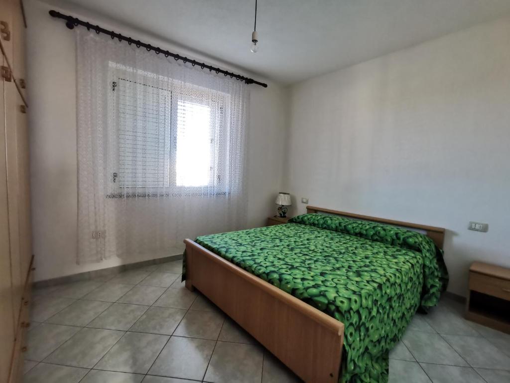 a bedroom with a bed with a green comforter and a window at Casa Maria in San Teodoro