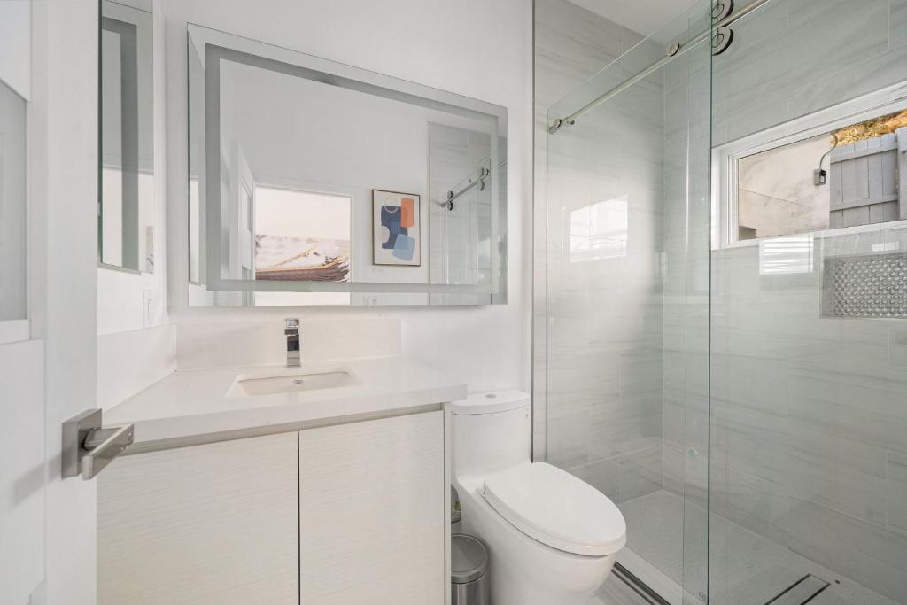 a white bathroom with a toilet and a glass shower at Pacific Coast Suites - Oceanfront Living in Los Angeles