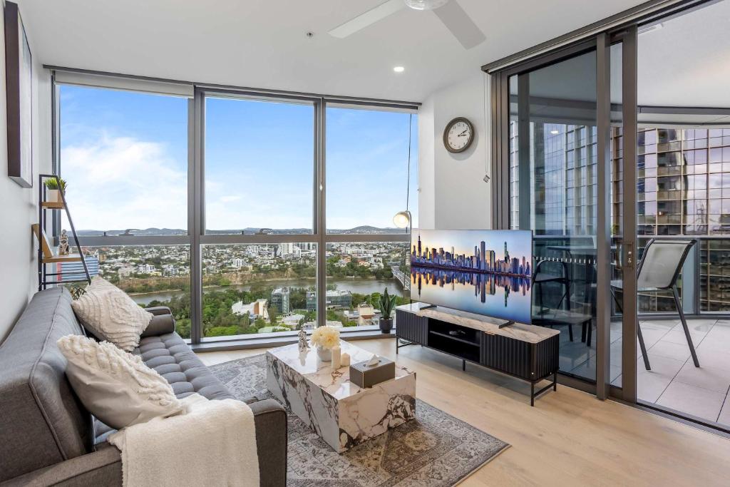 a living room with a couch and a tv and large windows at Your QW Escape - Pool Gym & Stunning Sky Deck View in Brisbane