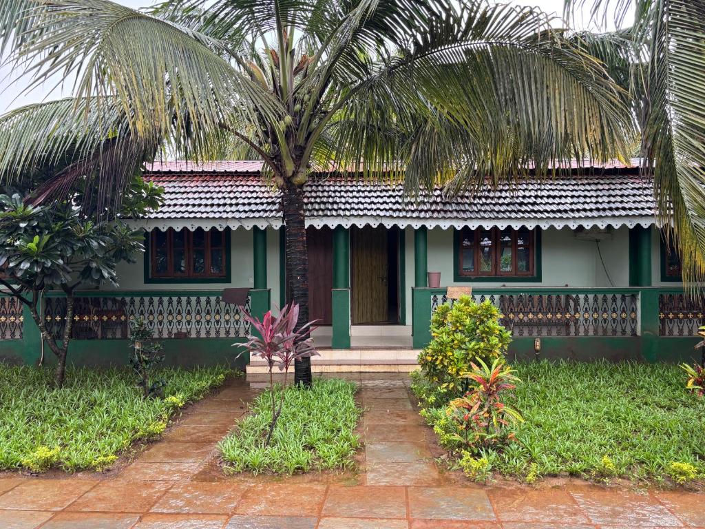 a green house with a palm tree in front of it at Golden Pearl Beach Resort in Baga