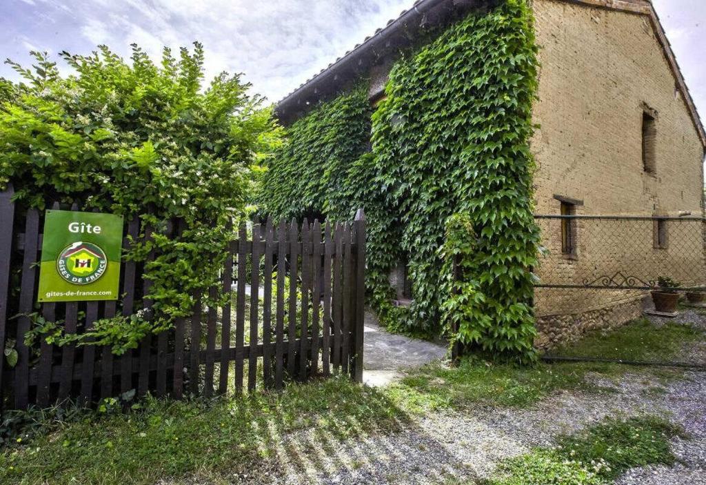 an ivy covered building with a fence and a sign at L'atelier du huchier in Poucharramet
