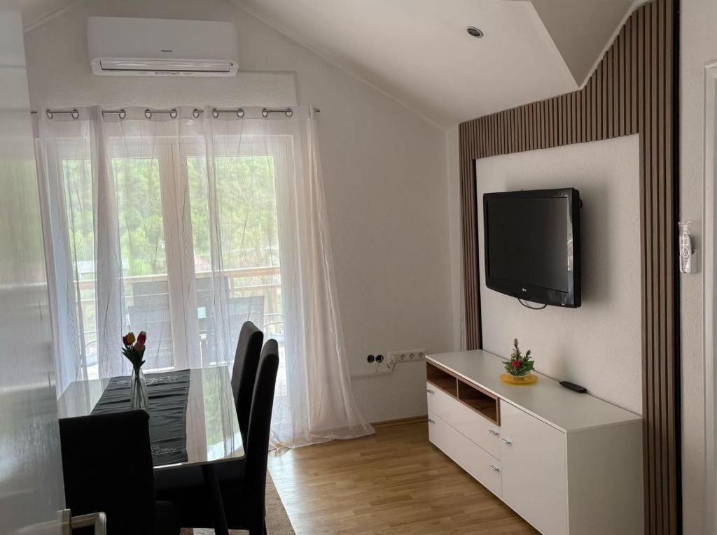 Un comedor con una mesa y un televisor y una ventana. en Apartmani D&D, en Jajce