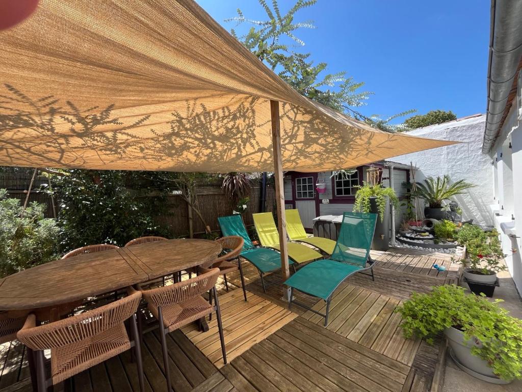 una terraza de madera con mesa, sillas y sombrilla en Au Coeur du Fief Naton, en Le Château-dʼOléron