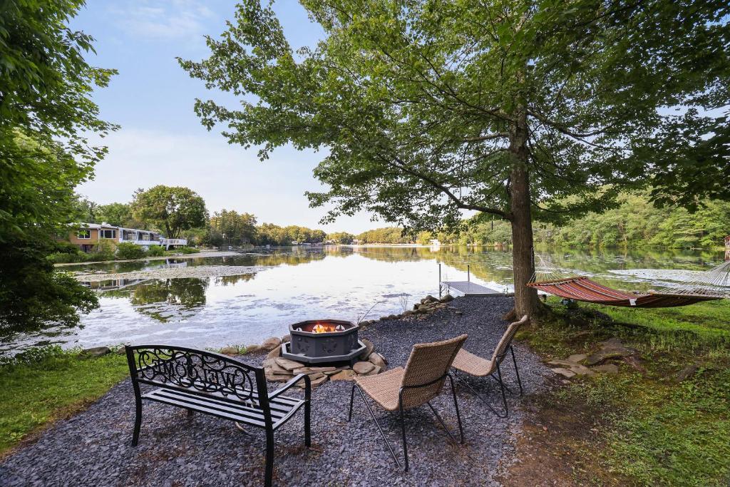 eine Feuerstelle mit zwei Stühlen und einer Hängematte neben einem See in der Unterkunft Lakeside Haven, a Modern Cottage with Lake Views in Effort