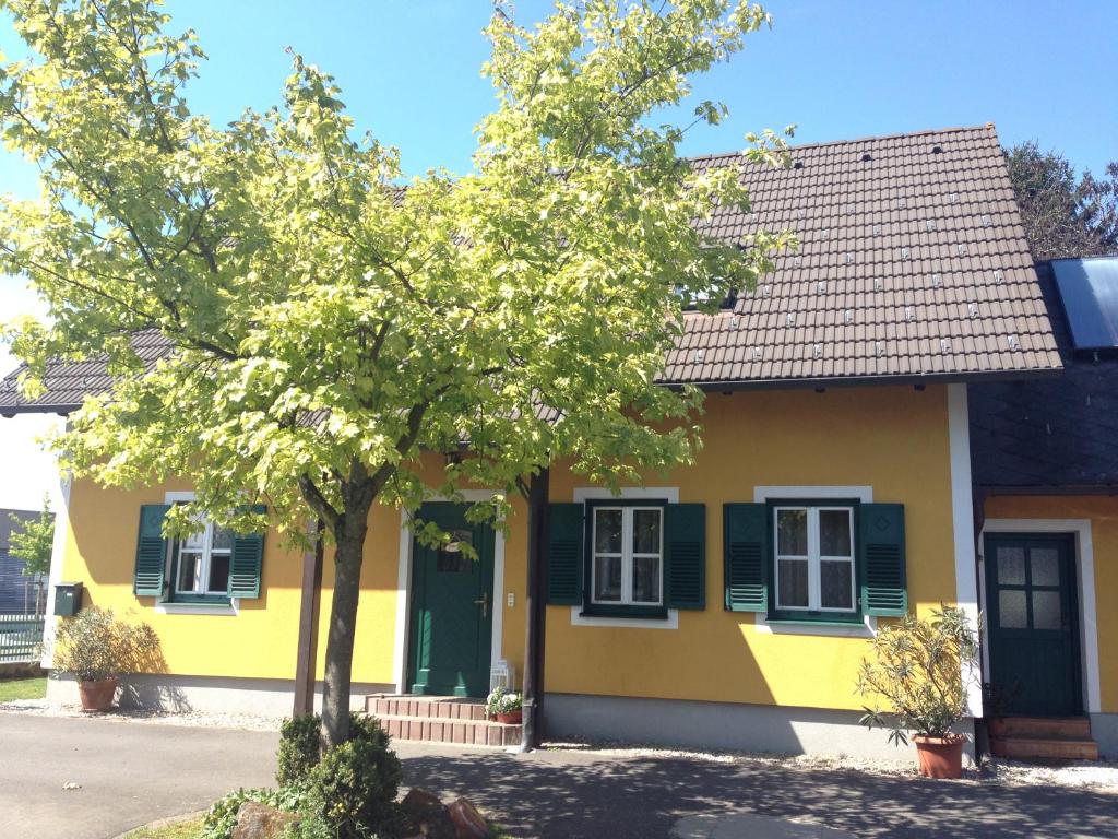 a yellow house with green shutters and a tree at Stefflhof in Gabersdorf