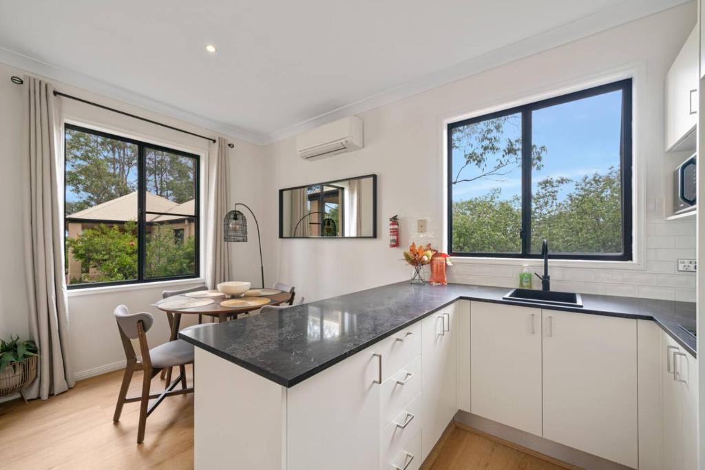 a kitchen with white cabinets and a table and two windows at Hunter Valley Prime Getaway in Pokolbin