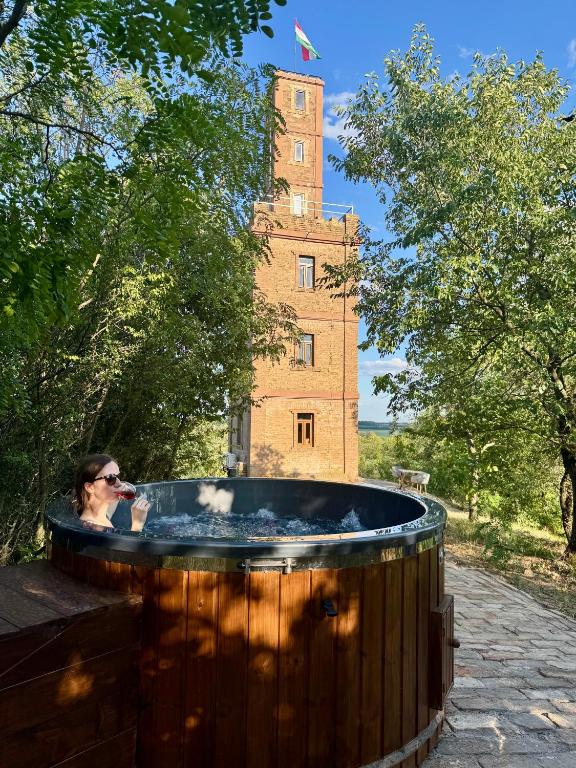 a woman standing in a hot tub in front of a building at Söréttorony - A jakuzzis erdei szállás in Kölesd