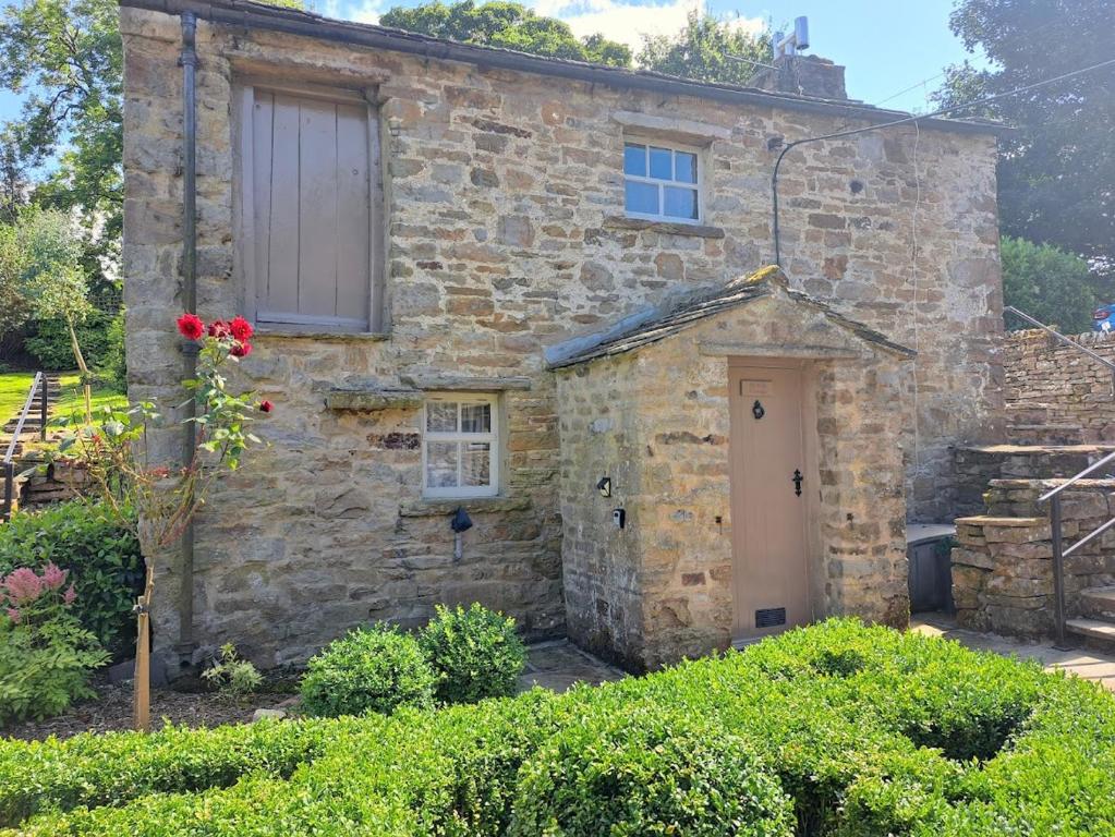 an old stone house with a white door at Beebole Cottage in Askrigg