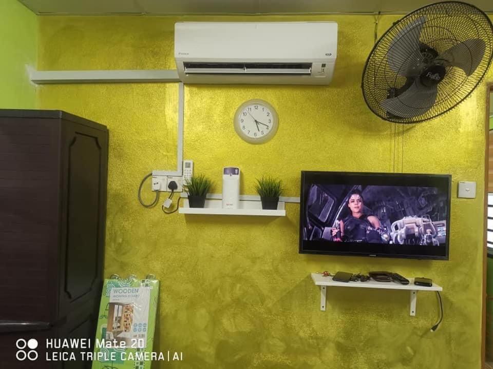 a tv on a yellow wall with a clock and a fan at Syedeyina Roomstay in Kangar