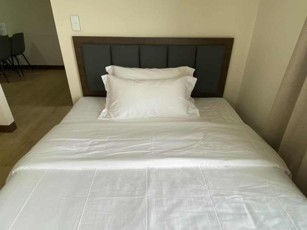 a white bed with a wooden headboard and white pillows at Cozy Stay with 2beds-Gentry 2mins to Okada- 6B in Sampong