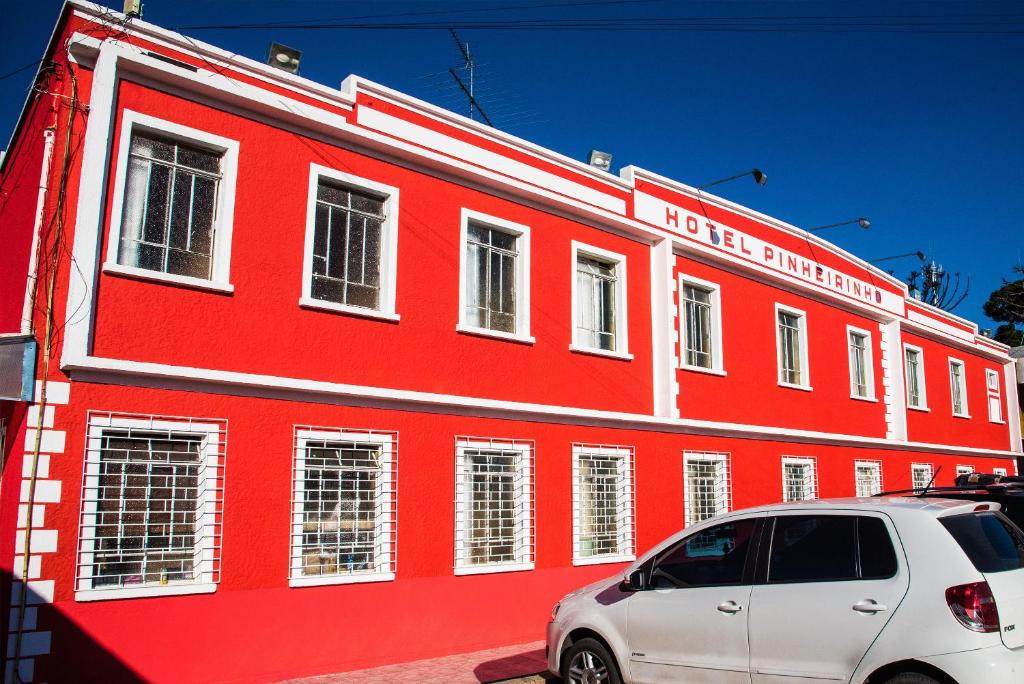 un edificio rojo con un coche blanco aparcado delante de él en Hotel Pinheirinho, en Curitiba