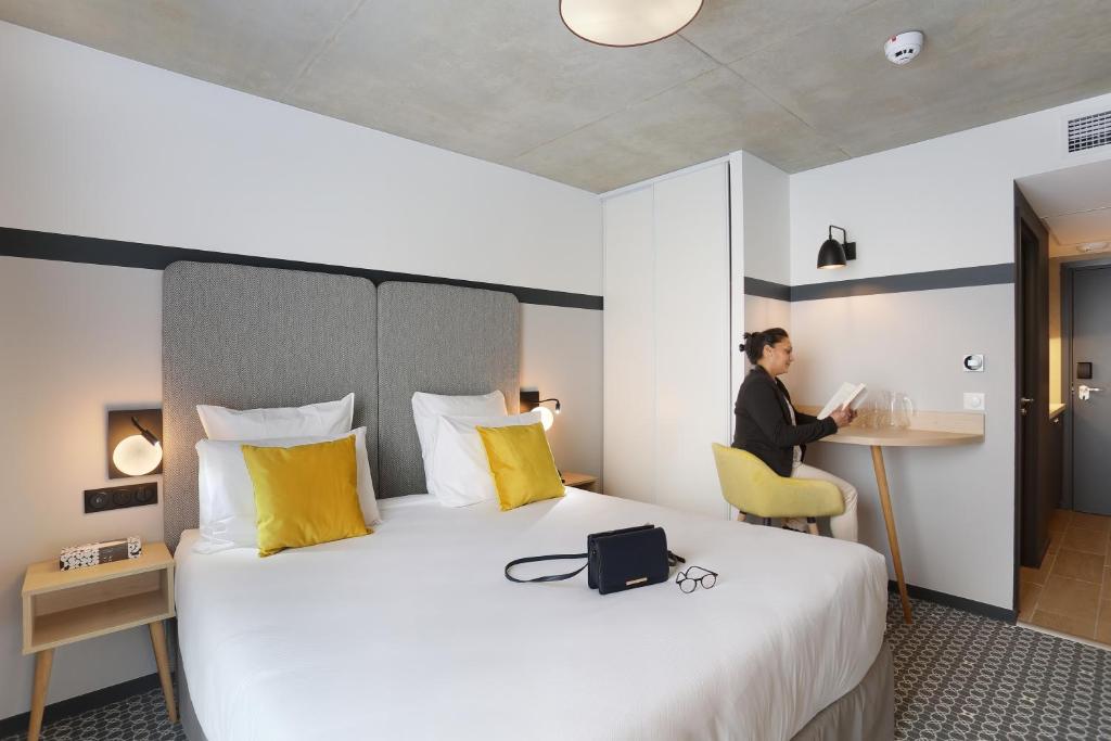 a woman sitting at a desk in a hotel room at Appart Hotel Odalys City Toulouse Blagnac Aéroport in Blagnac