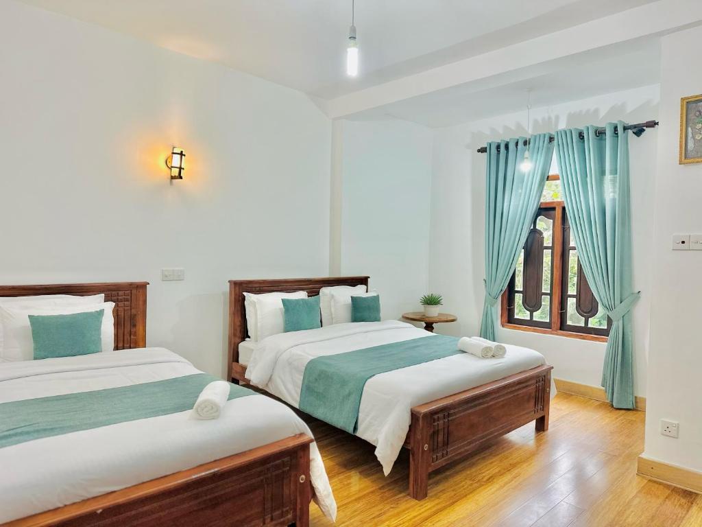 two beds in a bedroom with blue curtains at Highest Village Bungalow in Nuwara Eliya