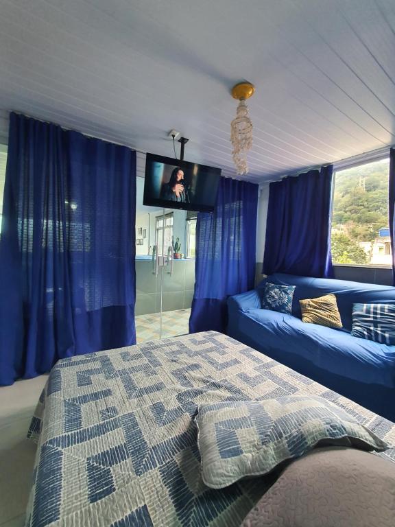 1 dormitorio con cortinas azules, 1 cama y TV en Suite Bela vista Muriqui Cantinho Feliz, en Mangaratiba