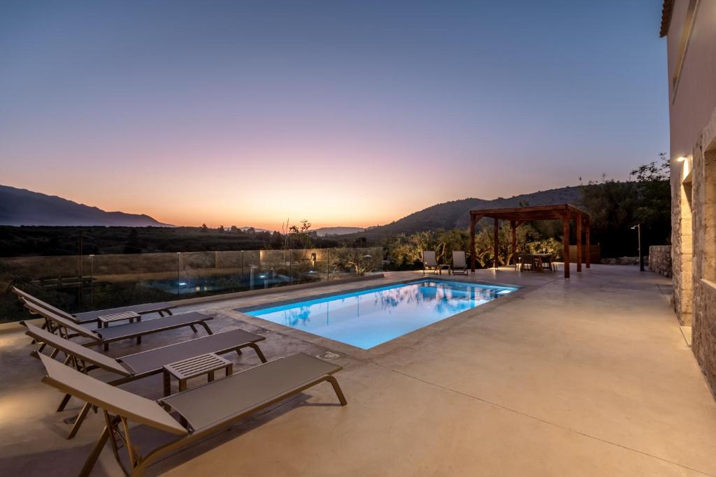 - une piscine avec des chaises et un coucher de soleil en arrière-plan dans l'établissement Olive Hideaway Boutique Villa - Private Pool - 7 Pax -Pet Friendly, à Kalamitsi Amygdali