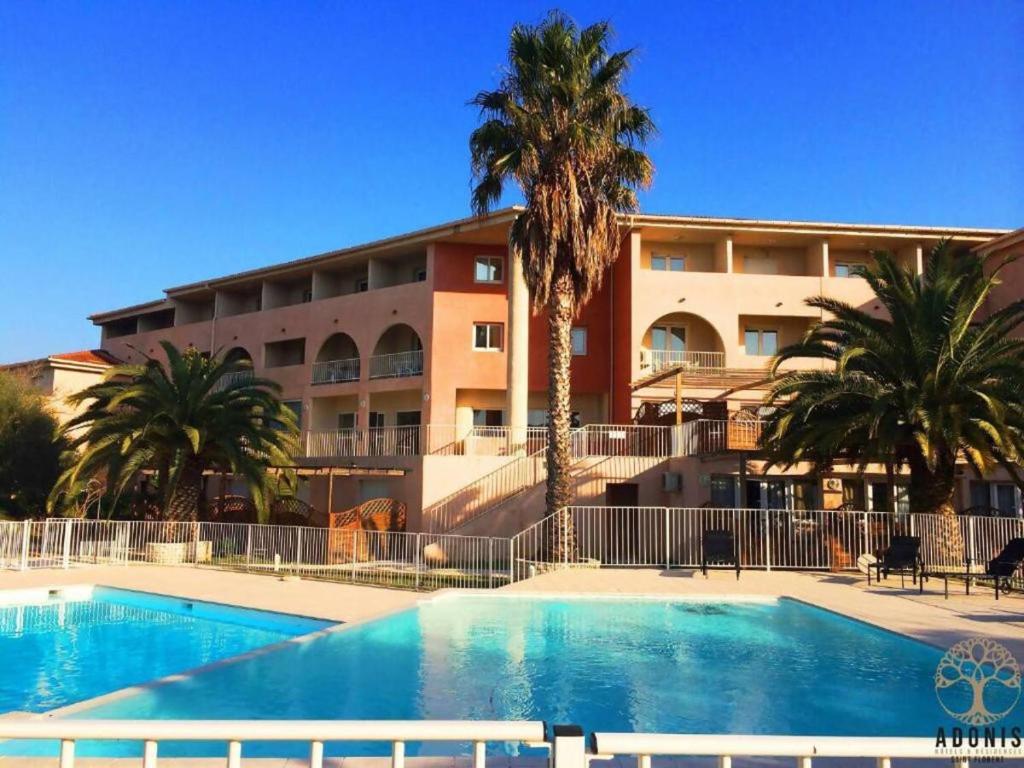 a swimming pool in front of a building with palm trees at Résidence la Citadelle in Saint-Florent