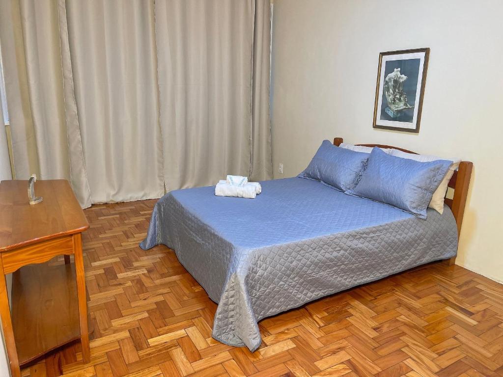 a bedroom with a bed with blue sheets and a wooden floor at Aconchego e comodidade no coração da cidade in Nova Friburgo