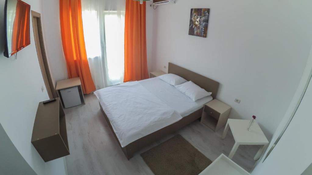 a small bedroom with a white bed and orange curtains at Hotel Atlantis in Eforie Nord