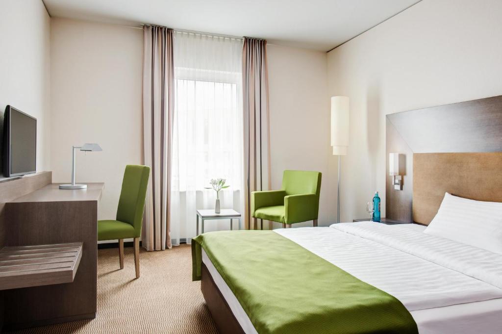 a hotel room with a bed and two green chairs at IntercityHotel Mainz in Mainz