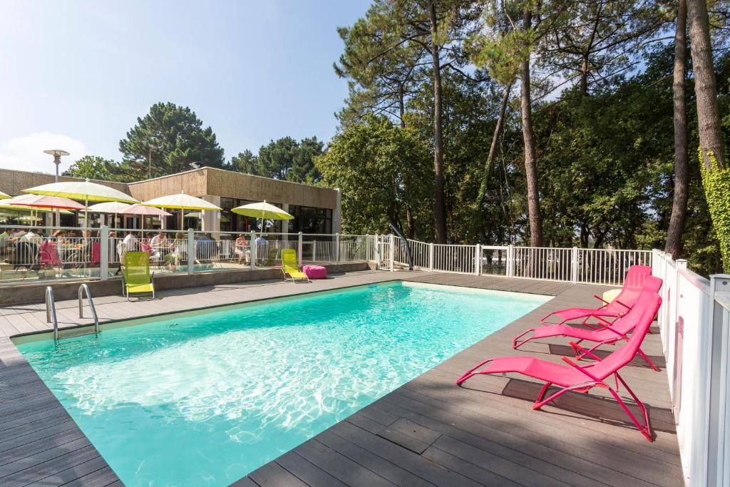 a swimming pool with pink chairs and umbrellas on a deck at Lorient Résidence in Caudan