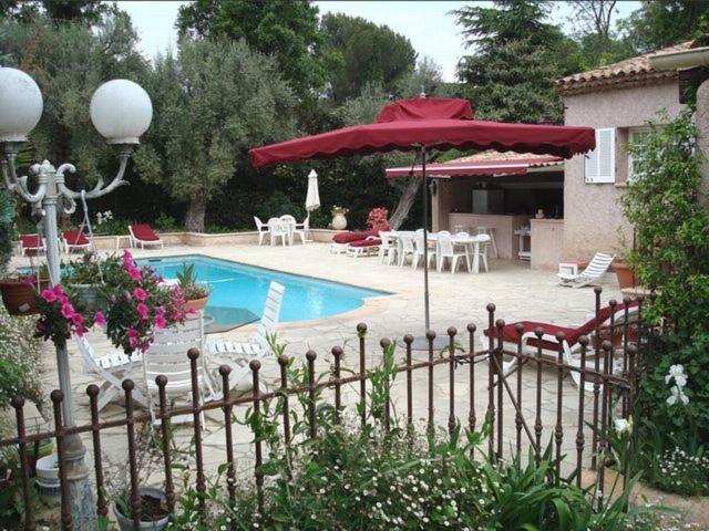 a pool with a red umbrella and chairs and tables at Villa l'Air du temps in Juan-les-Pins
