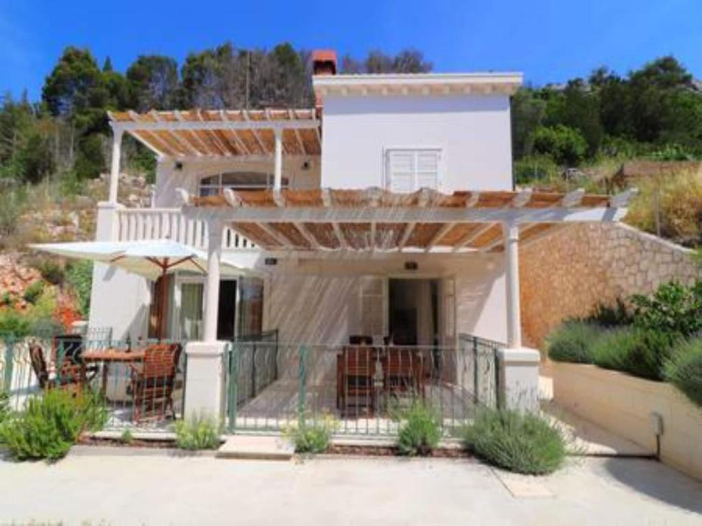 a white house with a balcony with an umbrella at Apartments Seafront Silence - One Bedroom Apartment with Terrace and Sea View in Trstenik