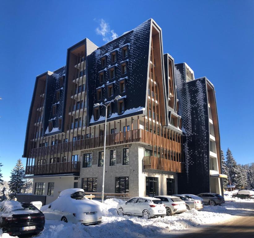 a building in the snow with cars parked in front at BiancaNeve Jahorina in Jahorina