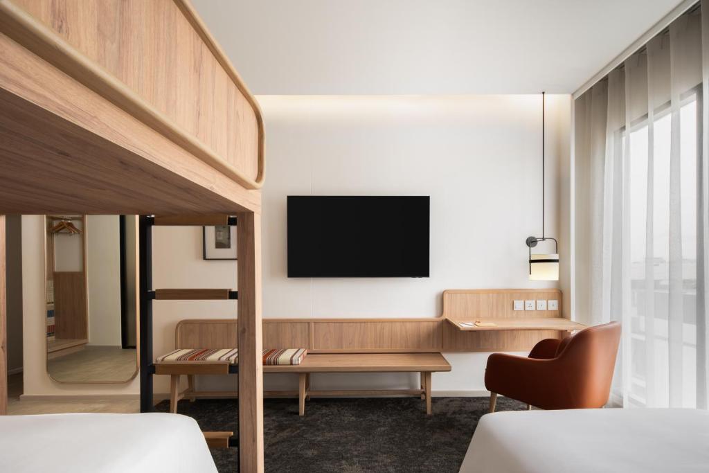 A twin-bed room with a wall-mounted TV, built-in desk, lounge chair, and full-height windows.
