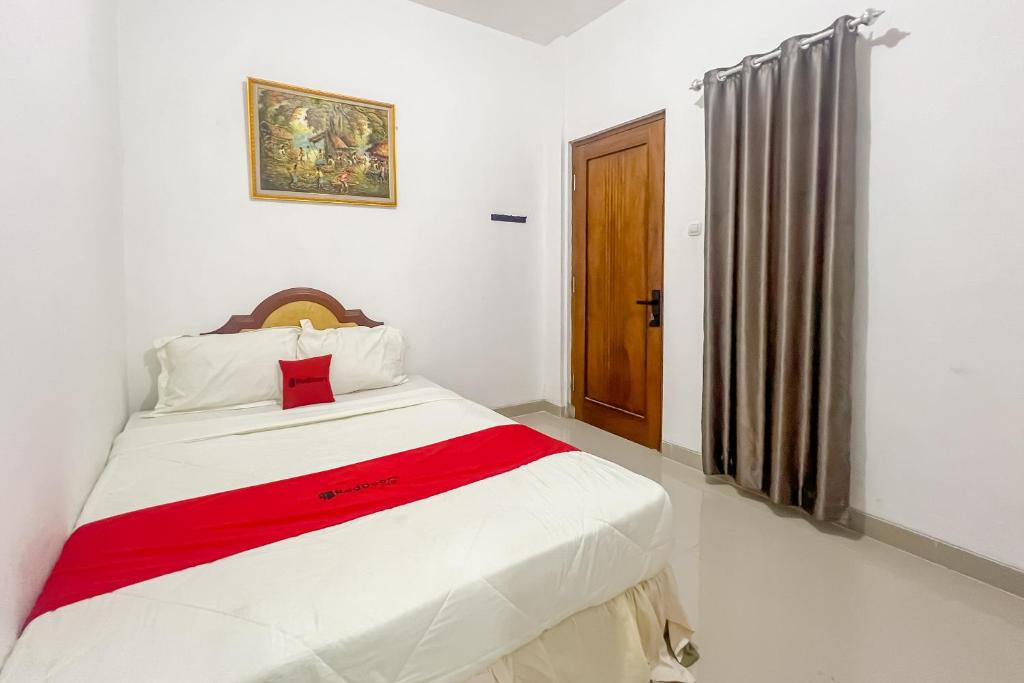 a bedroom with a white bed with a red blanket at RedDoorz at Dimens House Sragen in Sragen