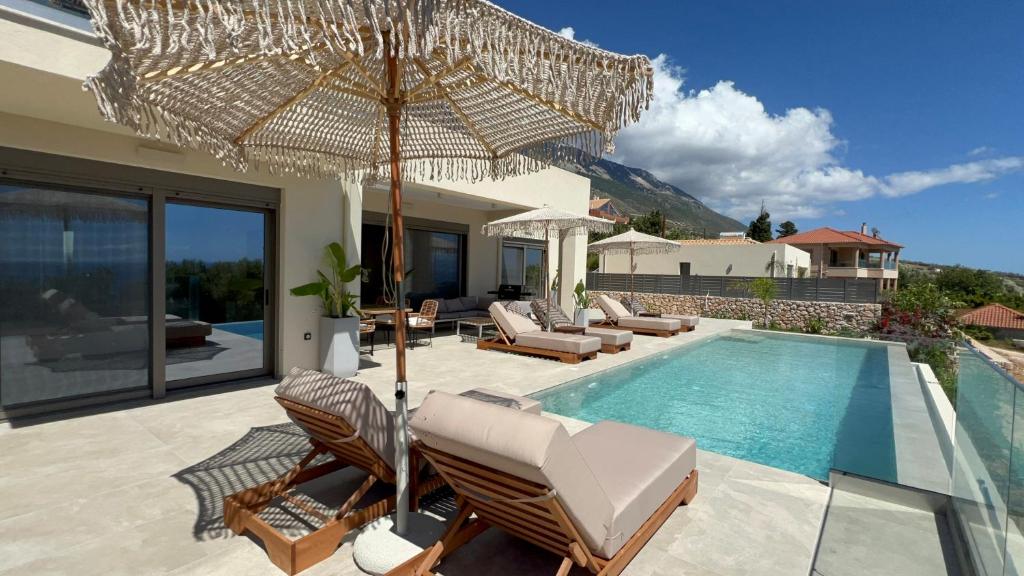 a patio with chairs and an umbrella next to a pool at Thalassasense villa lourdata in Kefallonia