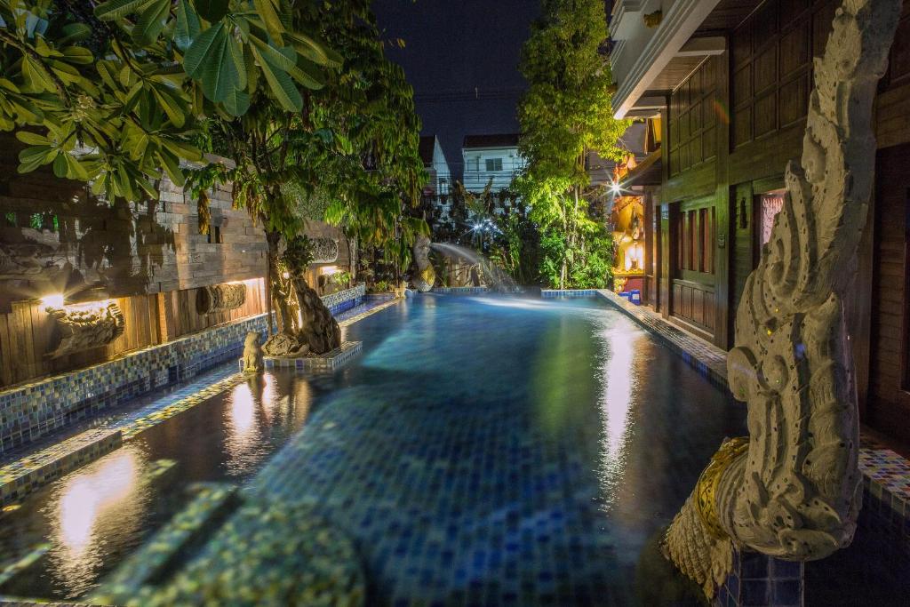 uma piscina à noite com árvores e edifícios em Singha Montra Lanna Boutique Style Hotel em Chiang Mai