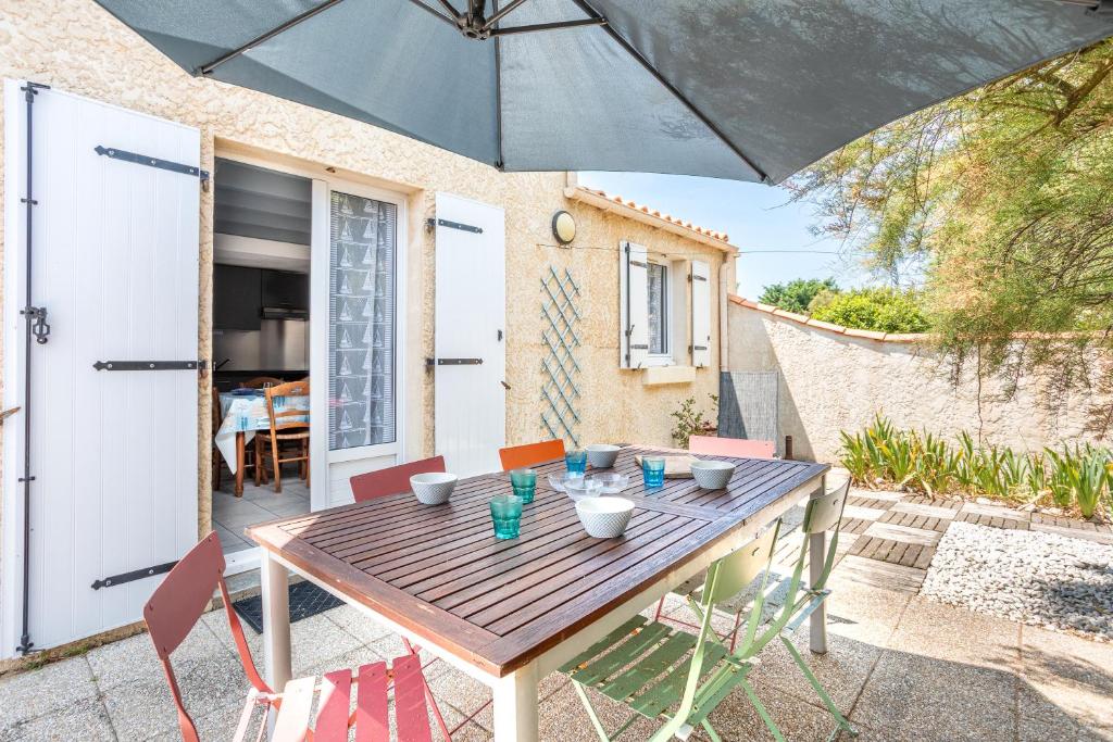 a wooden table with chairs and an umbrella at Maison avec Jardin proche Océan in Saint-Denis-dʼOléron
