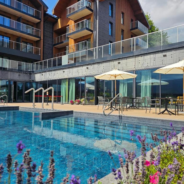 a swimming pool with tables and umbrellas next to a building at Happy Valley Resort Szklarska Poręba in Szklarska Poręba