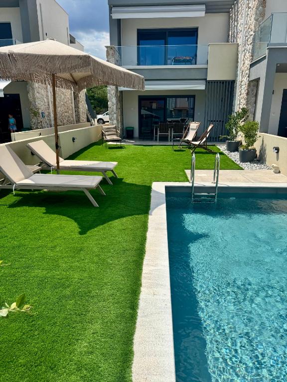 a backyard with a swimming pool with chairs and an umbrella at Trinity Pool Villas GOLD in Iraklitsa