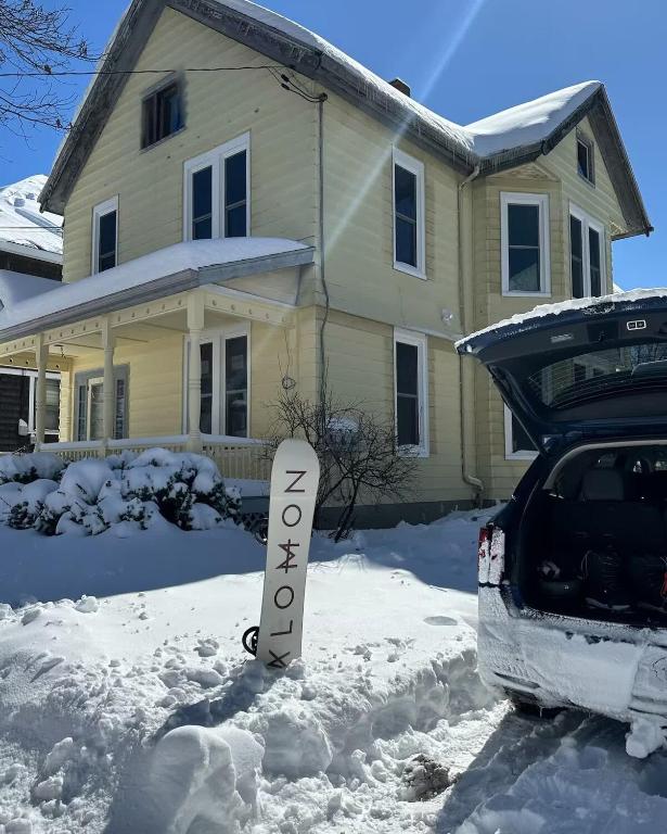 a snow covered house with a sign in front of a car at Spacious Central 4BR, Ski & Bike in Rutland