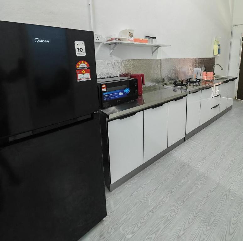 a kitchen with a black refrigerator and white cabinets at Singgoh Tido Homestay in Bukit Payong