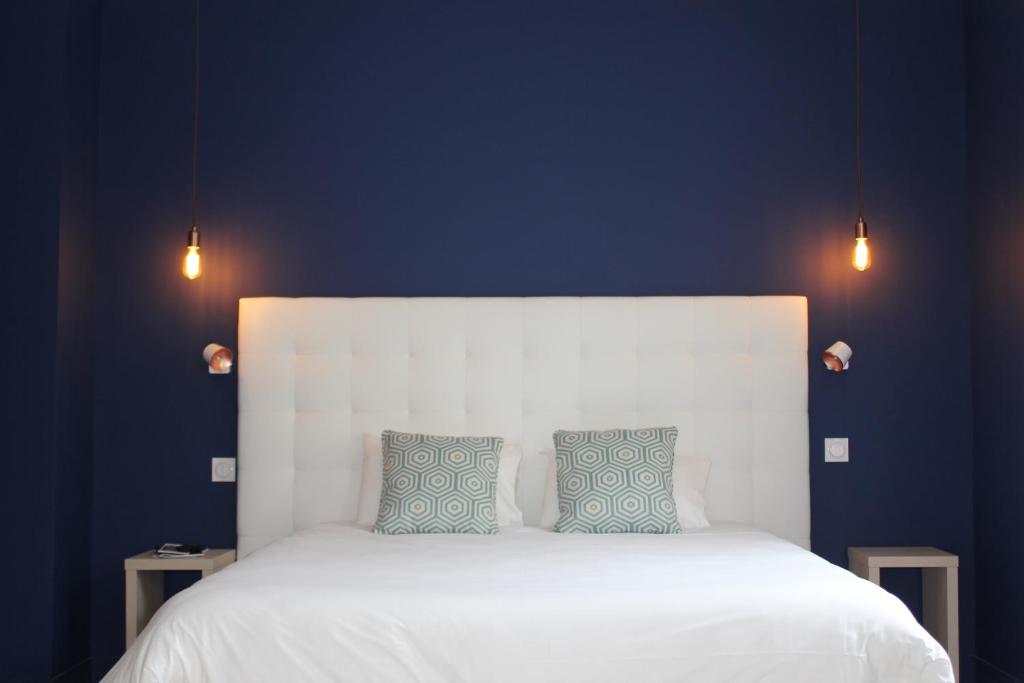 um quarto com uma cama branca e 2 almofadas azuis em Hôtel La Fontaine Caen Centre em Caen