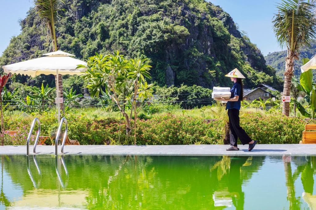 Eine Frau, die auf einem Bürgersteig neben einem Wasserkörper läuft. in der Unterkunft Trang An Ecorest Resort & Spa in Xuân Sơn