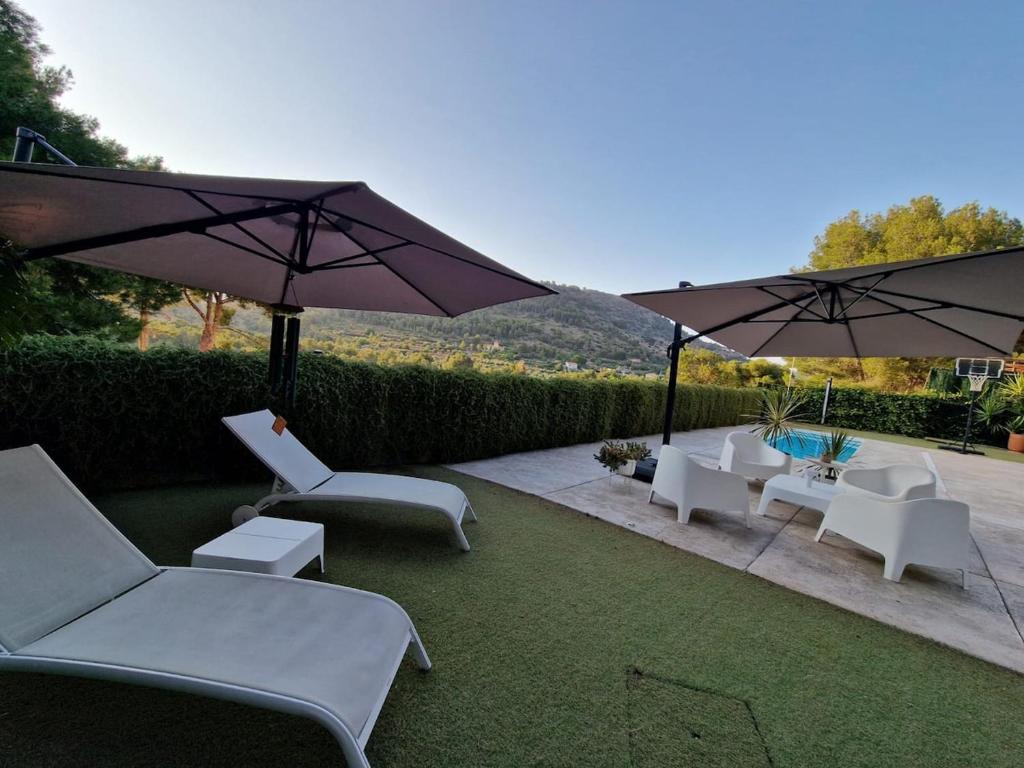 a patio with white chairs and umbrellas and grass at Parque Natural Sierra Calderona in Torres-Torres