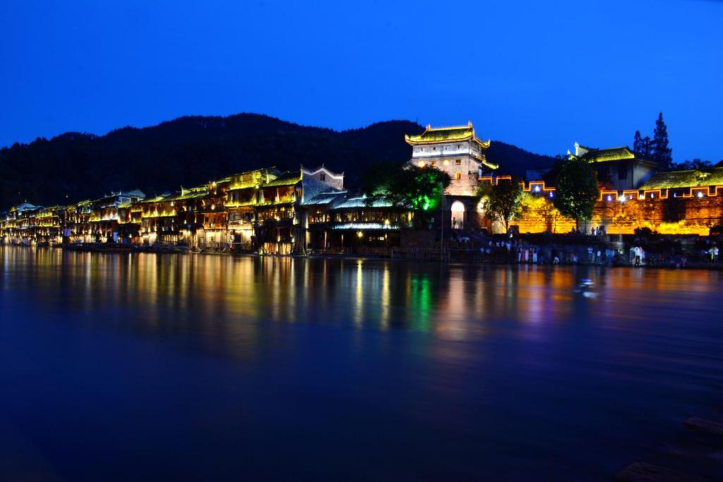 un gruppo di edifici sull'acqua di notte di Fenghuang Slowly Time Inn a Fenghuang