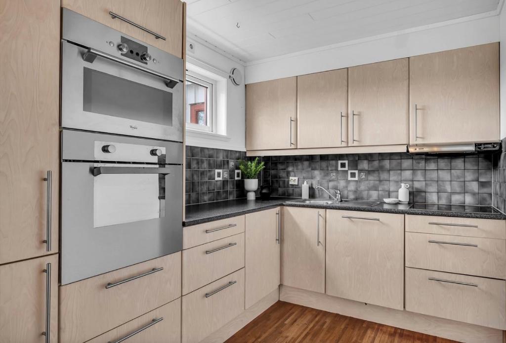 een keuken met houten kasten en roestvrijstalen apparatuur bij Romslig leilighet nært sentrum in Tromsø