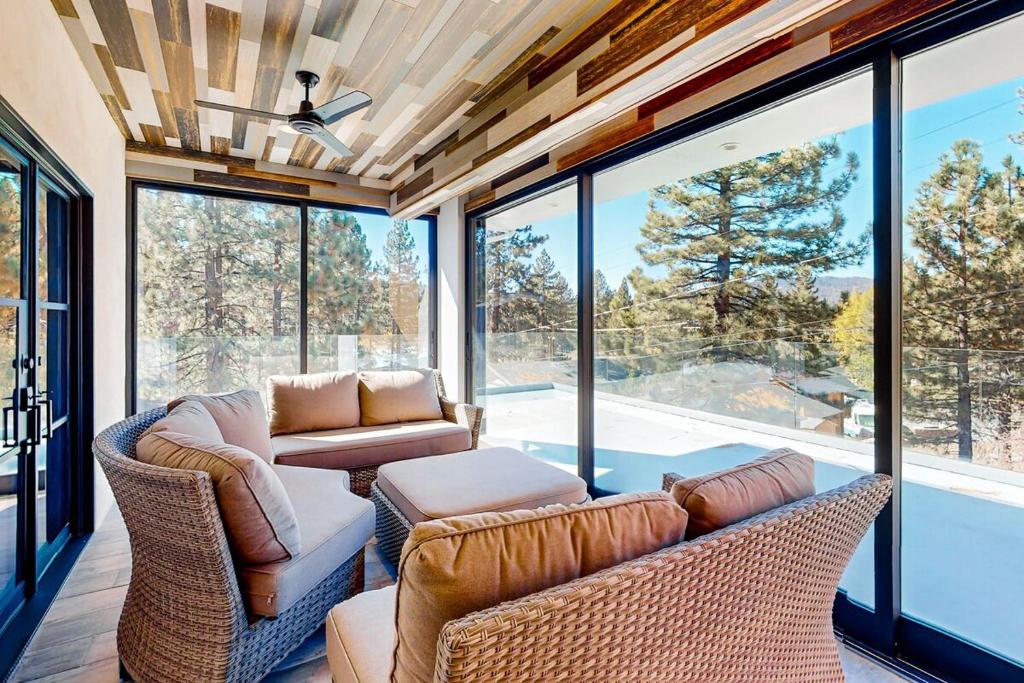 Una sala de estar con un sofá y sillas y ventanas. en Hillside Hideaway ~ Dog-friendly home with wraparound deck, grill, game room, & bar - walk to dining, en Big Bear Lake